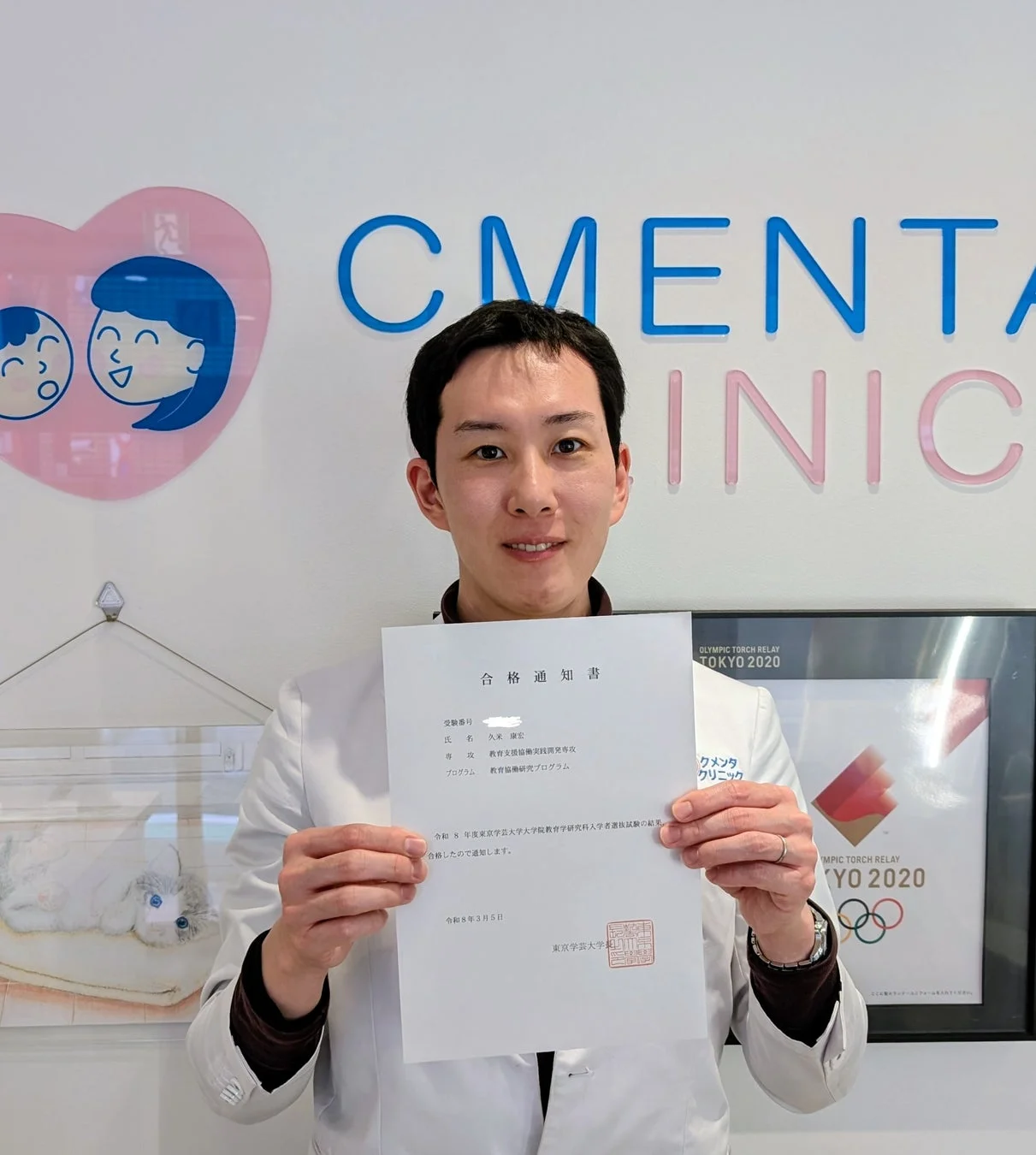 白衣姿で東京学芸大学大学院の合格通知書を掲げる久米康宏氏