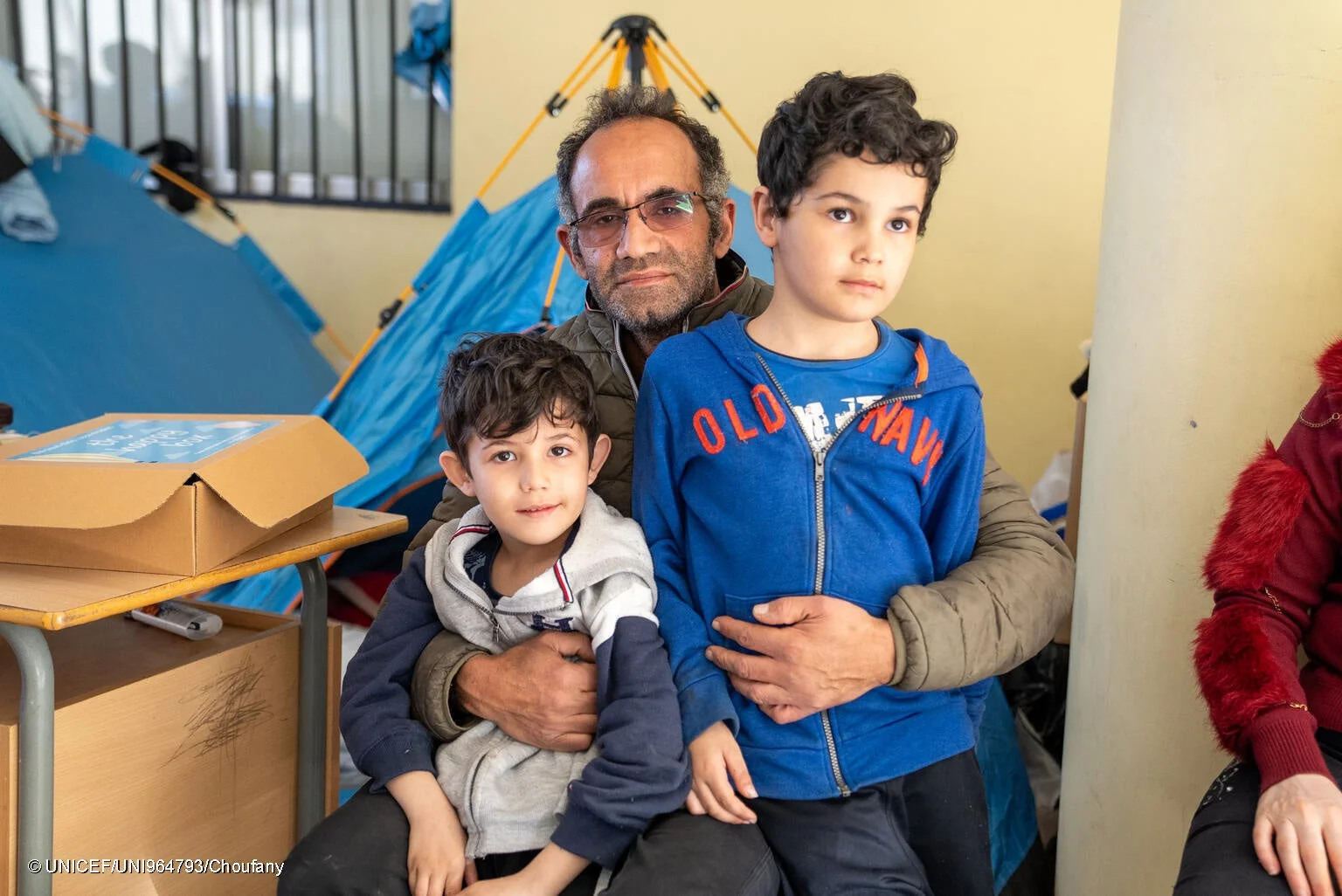 男性が2人の幼い息子を抱きかかえ、テントが見える