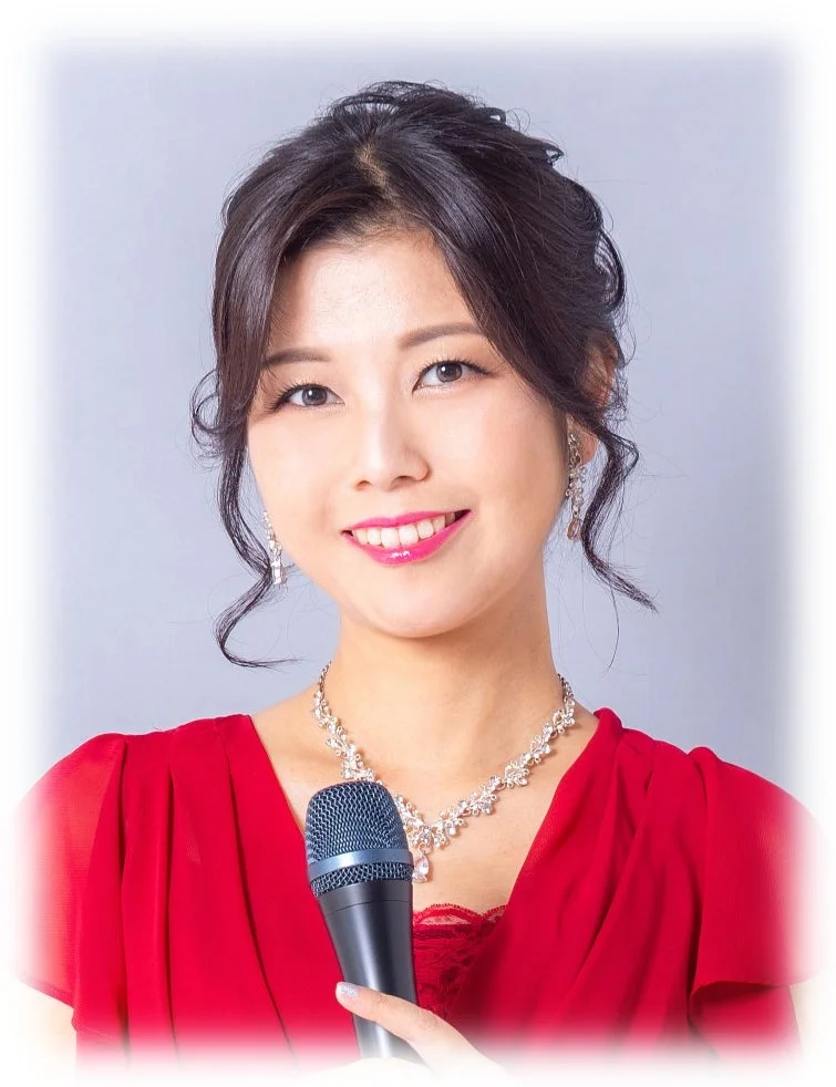 赤いドレスとアクセサリーを身につけ、マイクを持って笑顔でポーズをとる女性