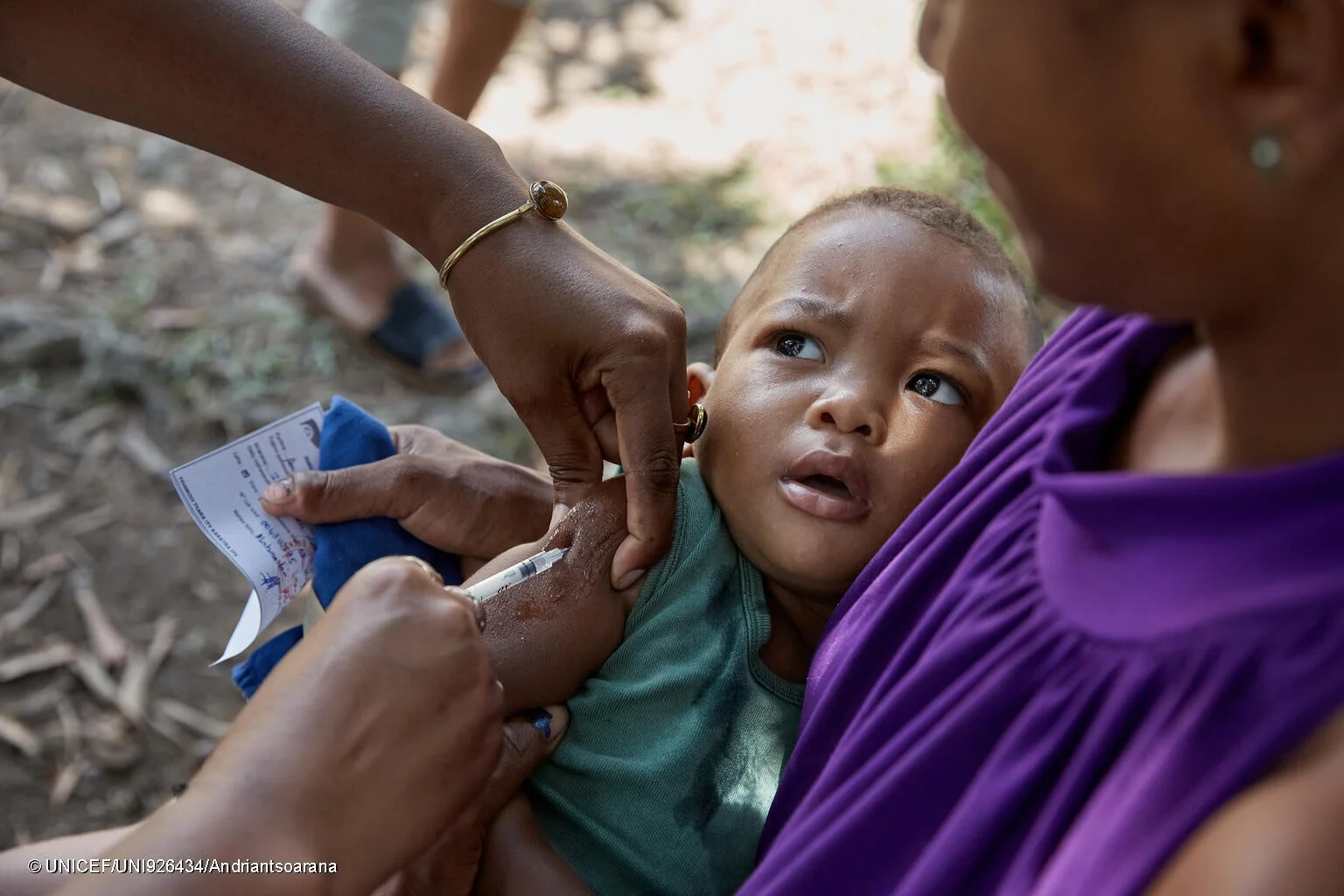 医療従事者が、抱っこされた赤ちゃんに予防接種を行っている場面。