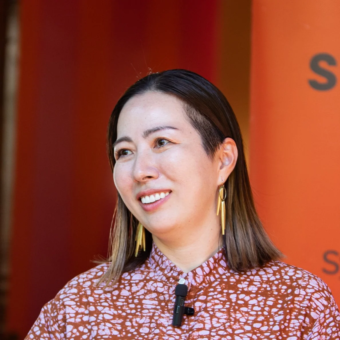 柄物のシャツを着てマイクをつけた笑顔の女性