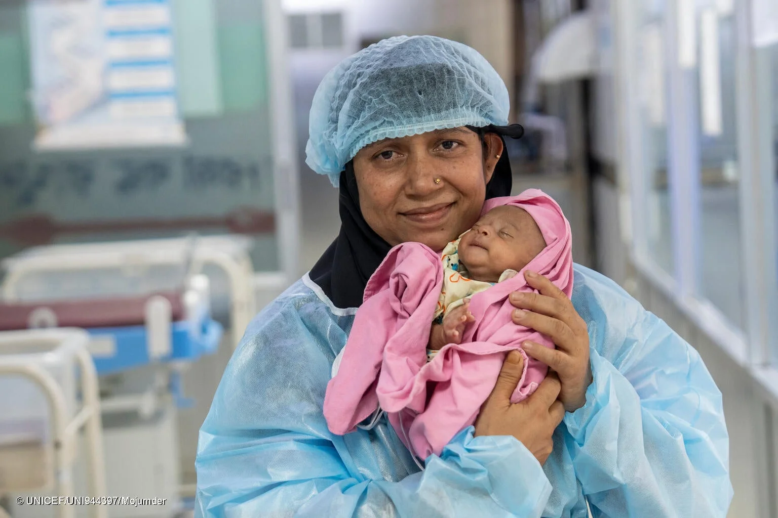 医療着を着た女性がピンクの布に包まれた新生児を優しく抱いている様子。