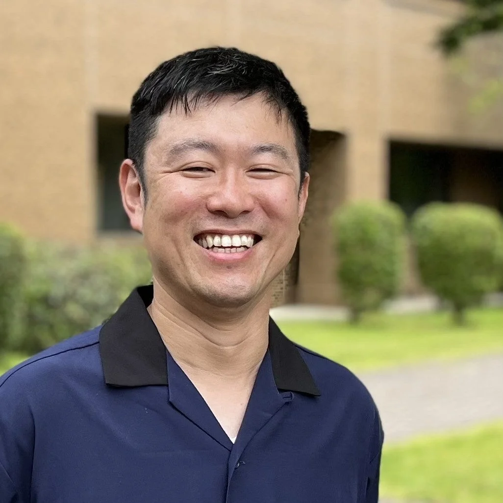 青いシャツを着たアジア人男性が屋外で満面の笑顔を見せているポートレート写真