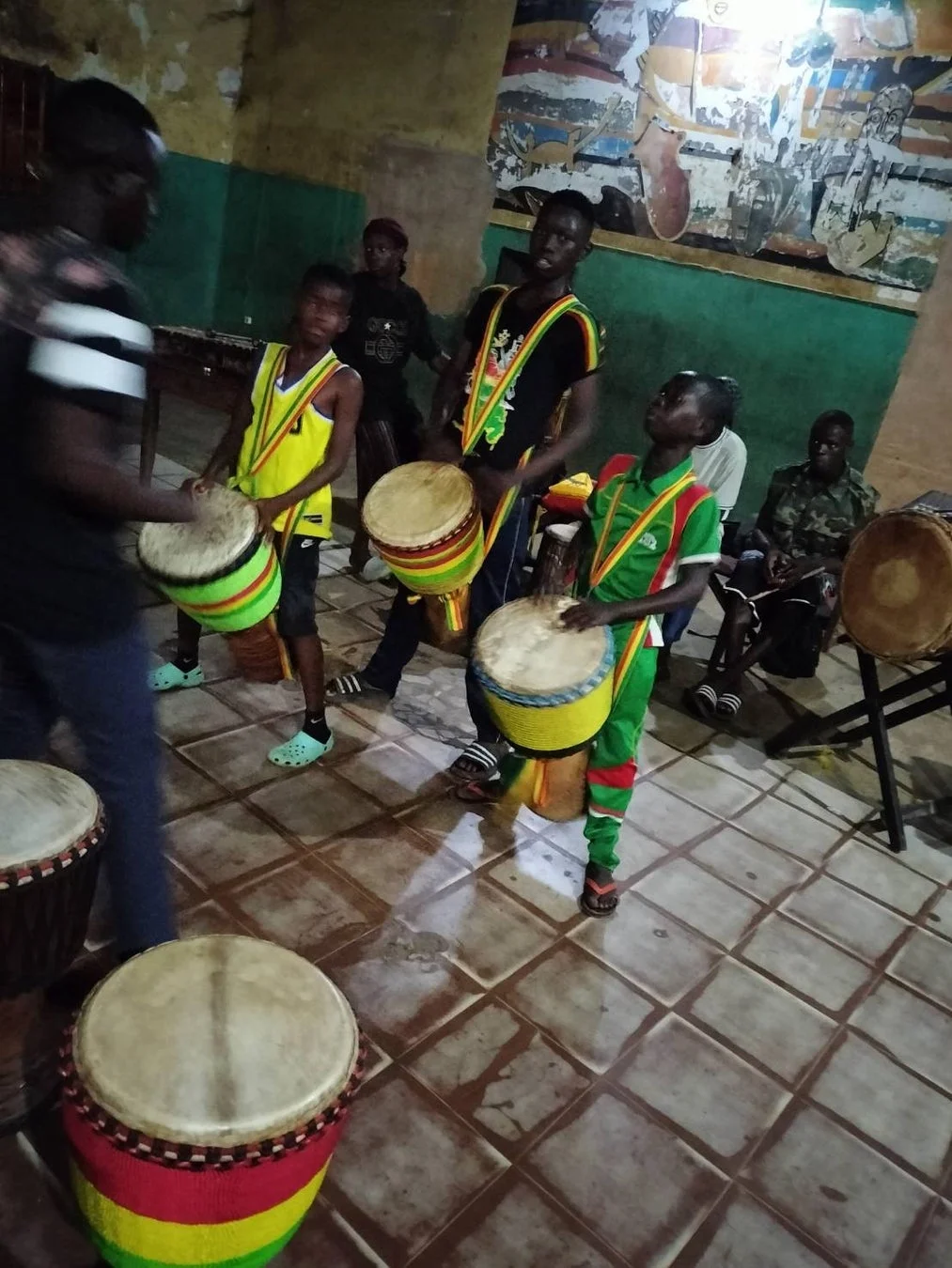 複数の少年や男性がジャンベドラムを演奏している屋内の様子です。