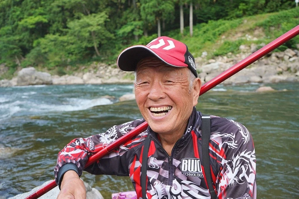 川辺で赤い帽子をかぶったシニア男性が満面の笑みを浮かべている