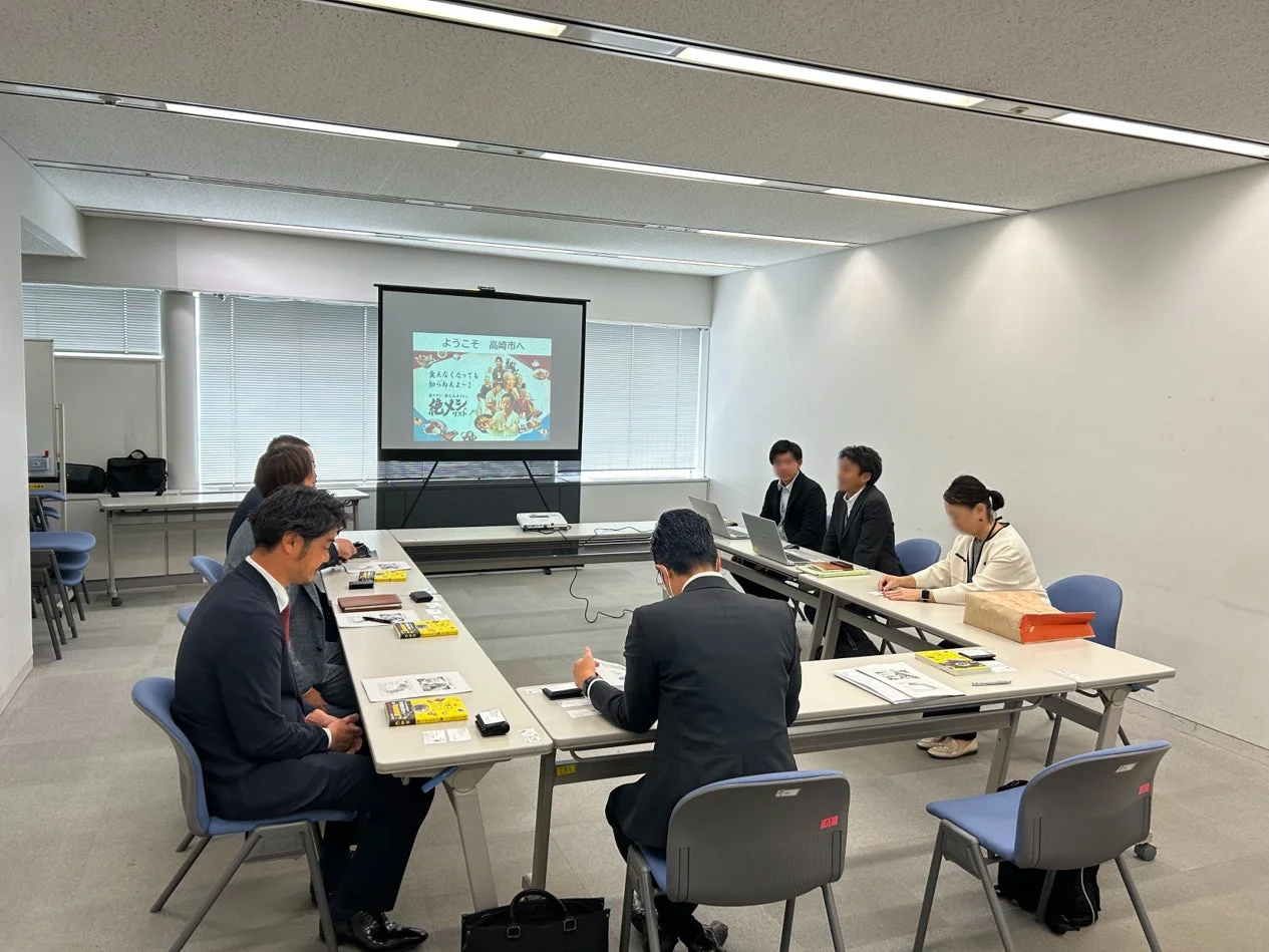 会議室で複数の参加者がプレゼンテーションを聞いています。