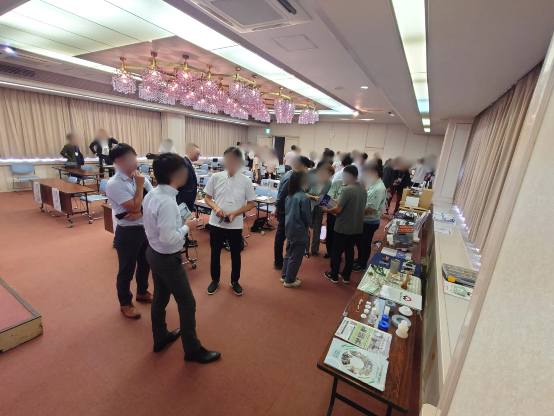 広々とした会場で多くの人々が集まり、展示された資料やサンプルを見ながら交流している様子です。