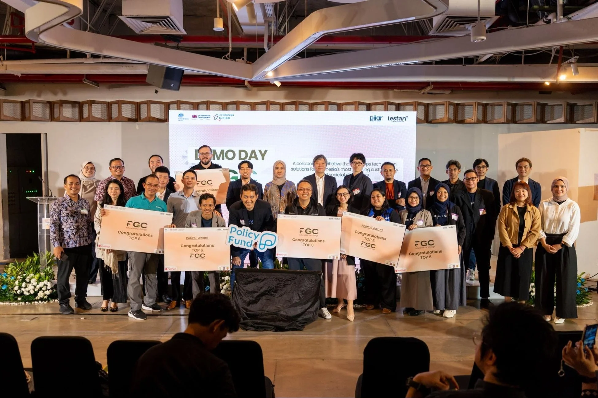 インドネシアの「DEMO DAY」イベントで、社会・環境問題解決に貢献するテクノロジーソリューションを開発したFGCとPolipoli Award受賞チームが、関係者と共に集合写真を撮っています。