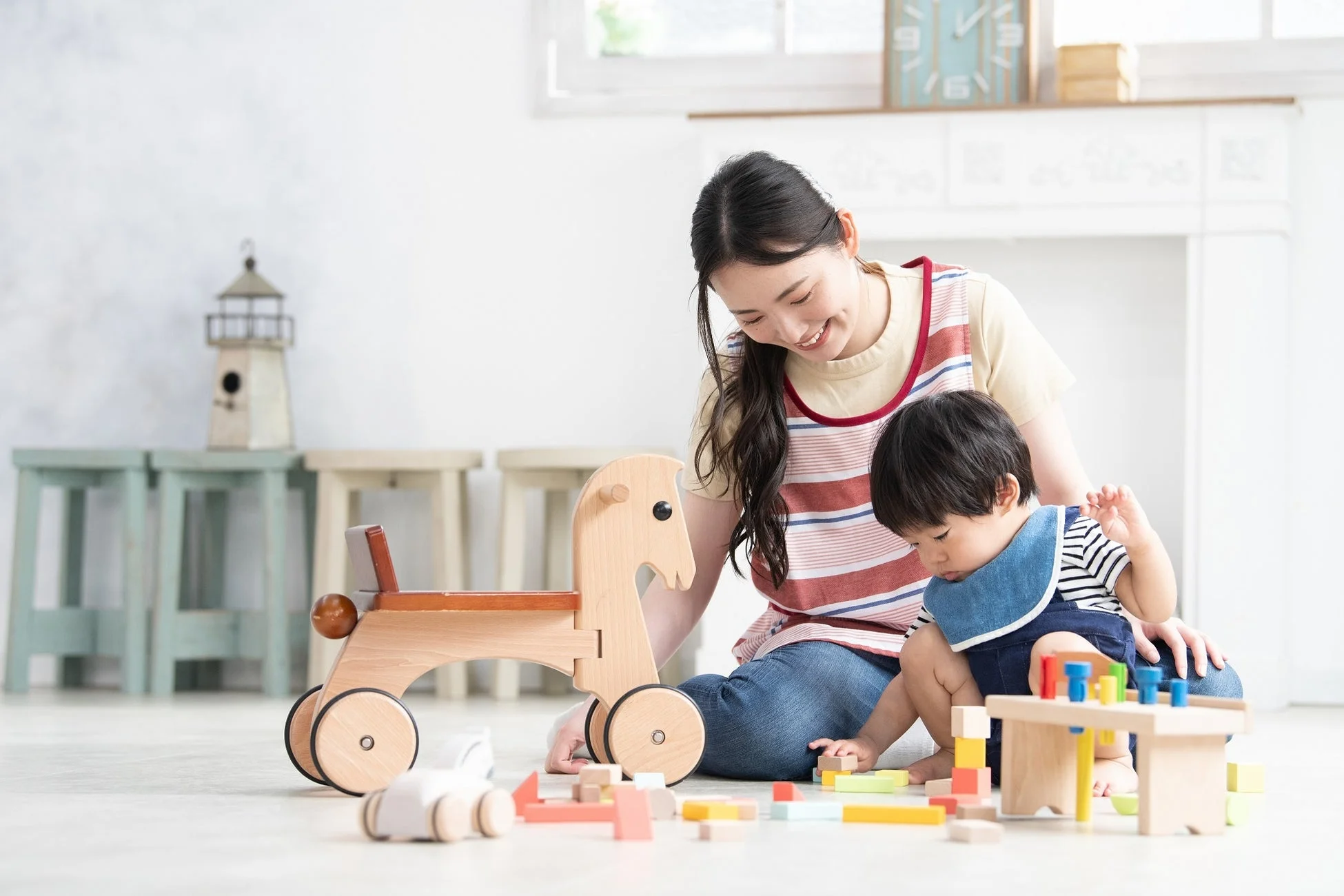 明るい部屋の床で、母親らしき女性と子供が木のおもちゃや積み木で遊んでいる様子