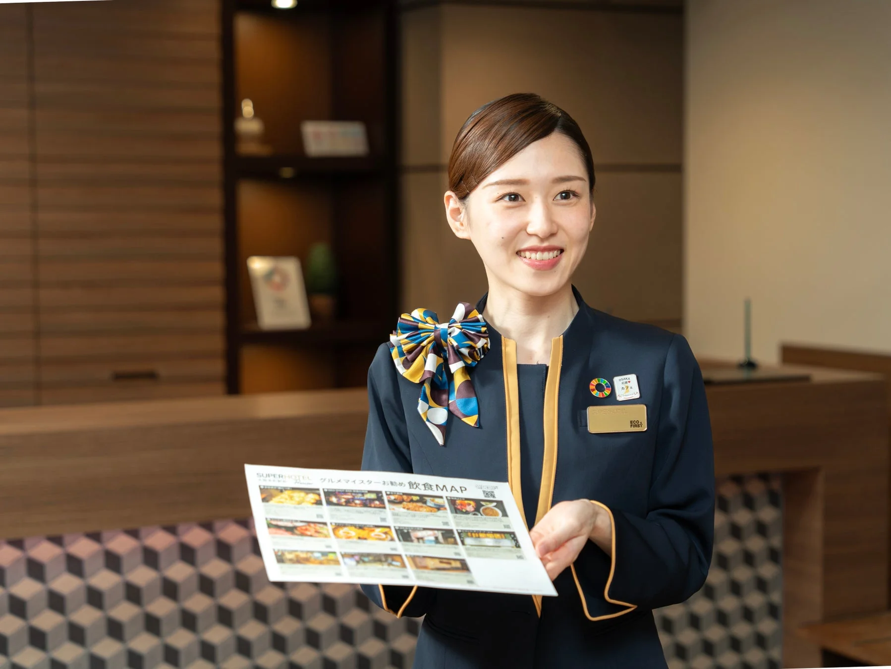 ホテルの女性スタッフがグルメ情報を紹介する飲食MAPを差し出す