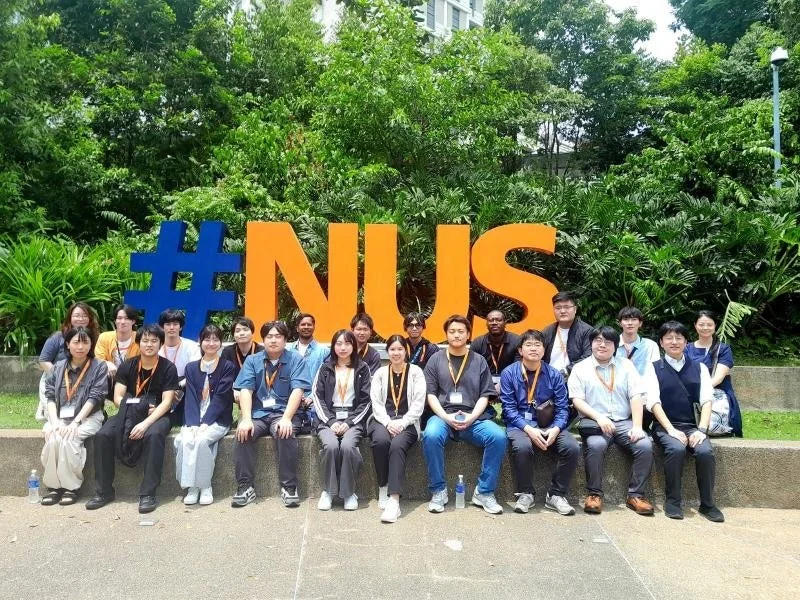 NUSのモニュメント前で集合写真を撮る学生たち