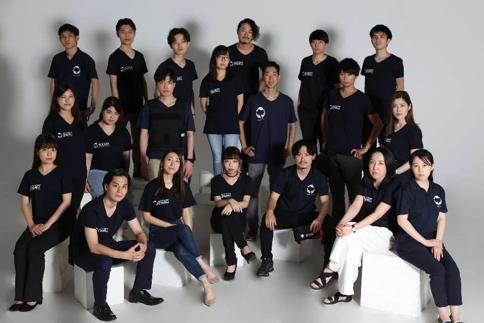 紺色のチームシャツを着用した約20名の日本人男女が、スタジオで撮影された集合写真