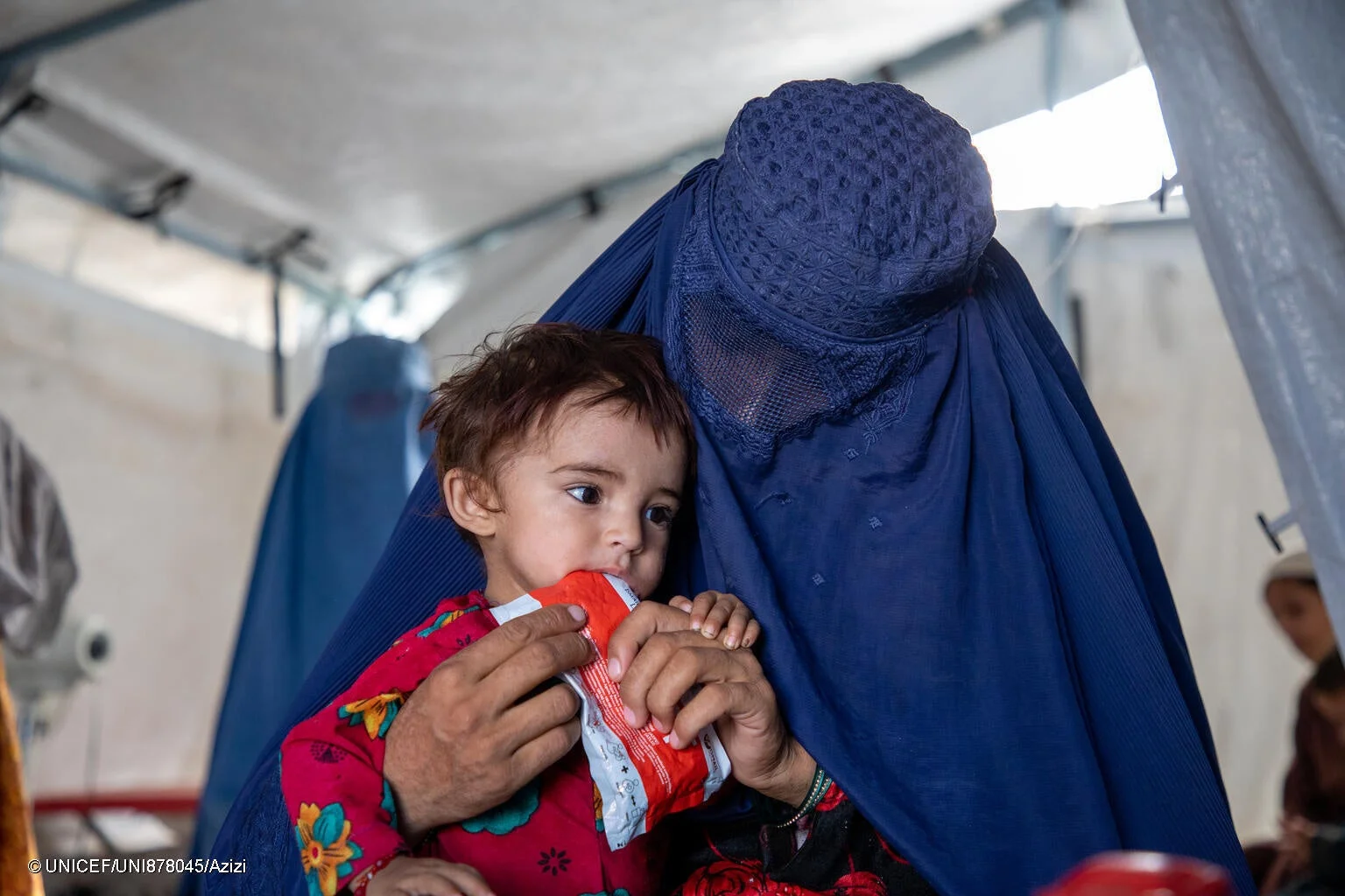 ブルカを着用した女性がテントの中で子供に栄養補助食品を与えている様子。