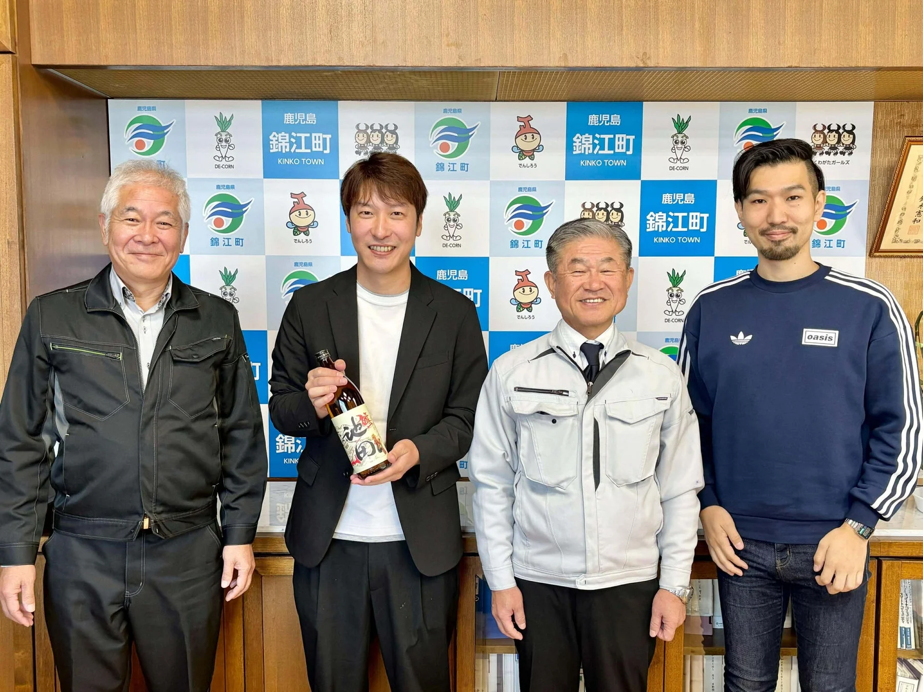 錦江町のPRパネルを背景に笑顔で並ぶ男性たち
