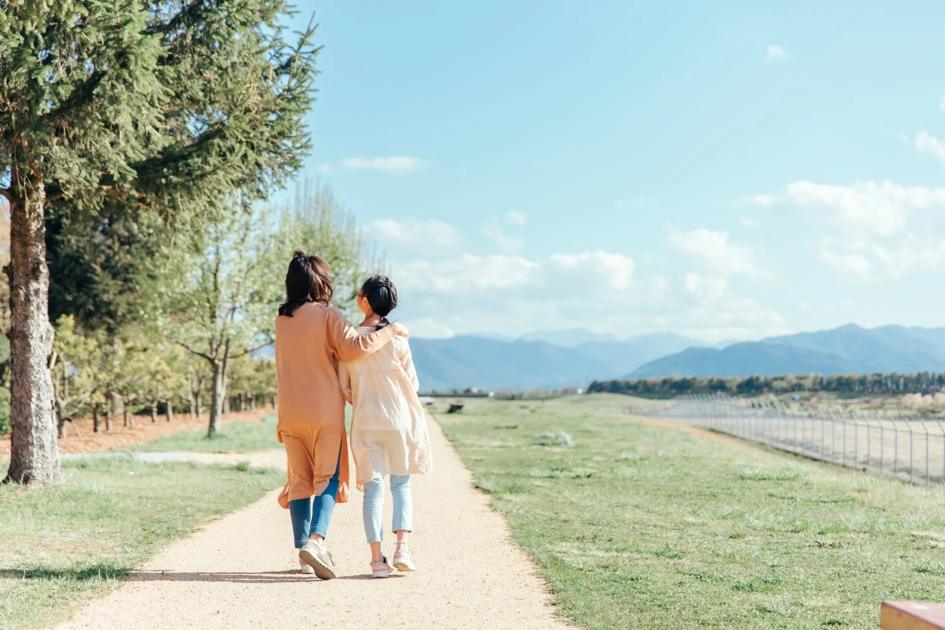 晴れた日の屋外で、肩を寄せ合いながら小道を歩く二人の後ろ姿
