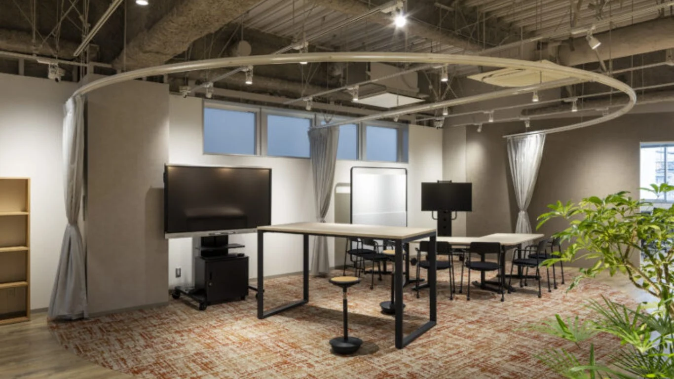 モダンなデザインのオフィス空間で、大画面ディスプレイや可動式のテーブル、椅子が配置されています。